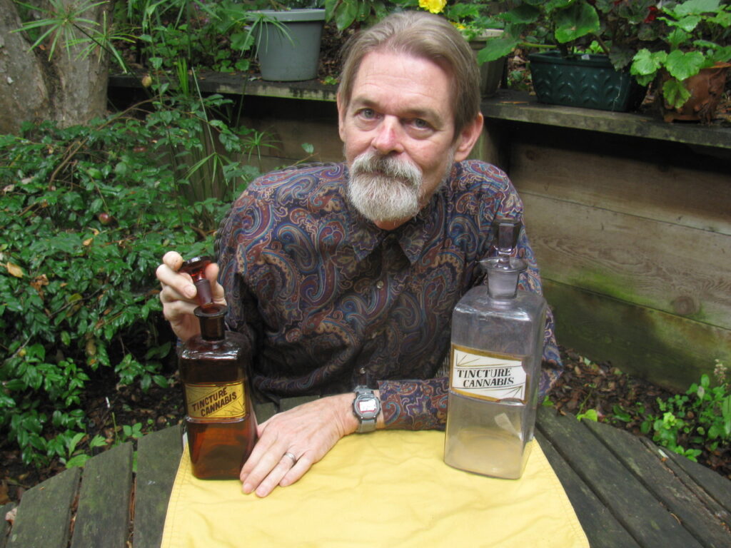 Dale Gieringer of California NORML posing with two large cannabis tincture bottles.