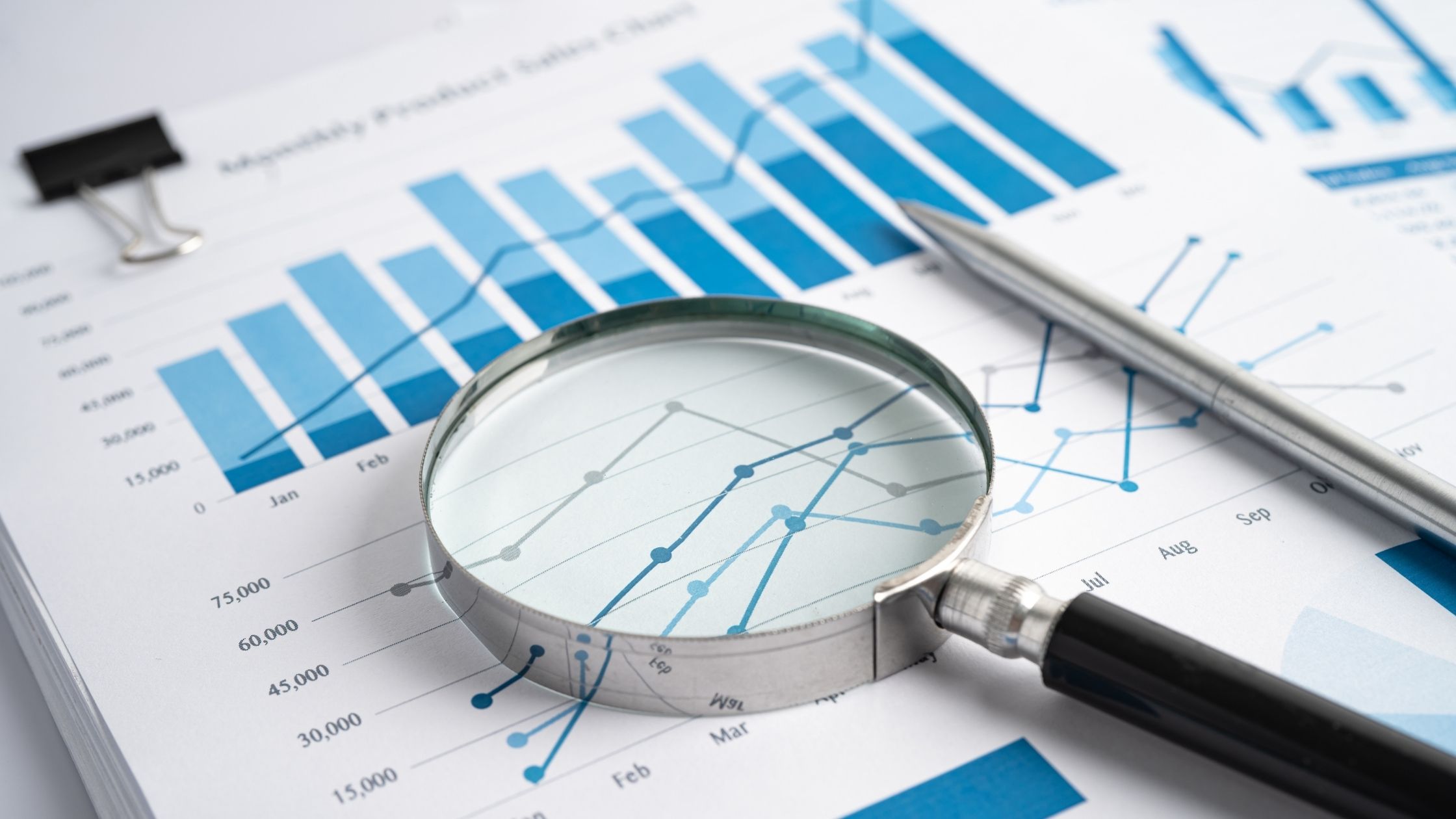 A magnifying glass sits on a piece of paper with charts and graphs